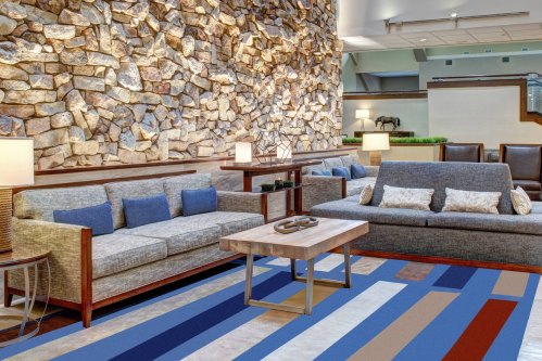 Modern lounge area featuring stone wall, two sofas, a wooden coffee table, and colorful patterned rug.