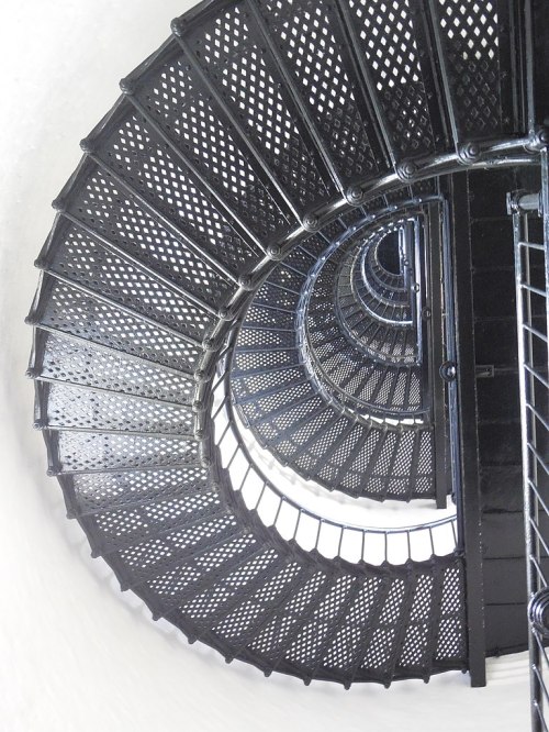 A spiral staircase viewed from above, featuring a black metal design and a circular pattern.