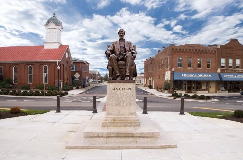 Statue of Abraham Lincoln seated on a pedestal, with buildings and a cloudy sky in the background.