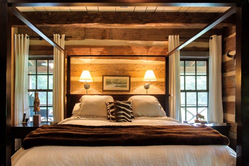 Cozy bedroom with a four-poster bed, wooden beams, soft lighting, and large windows overlooking nature.
