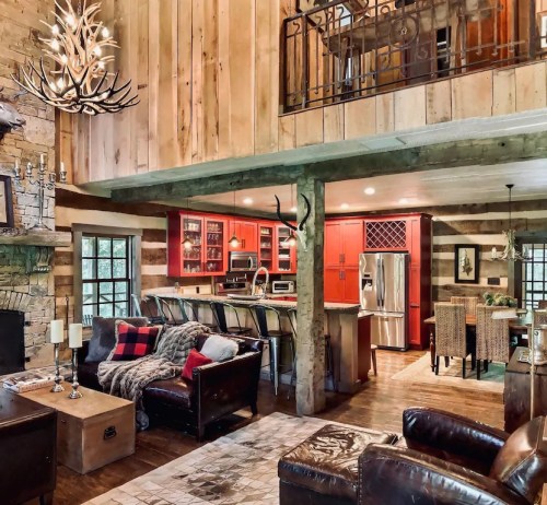 Cozy cabin interior featuring wooden walls, a stone fireplace, and a modern kitchen with red cabinets.