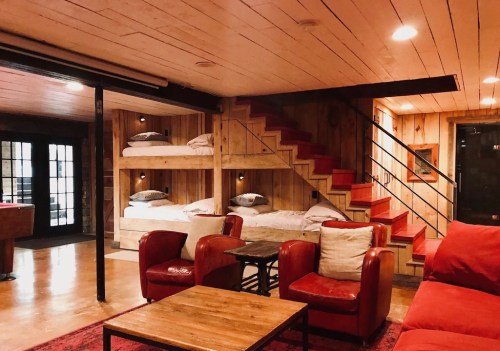 Cozy interior with wooden walls, bunk beds, a staircase, red chairs, and a coffee table in a warm, inviting space.