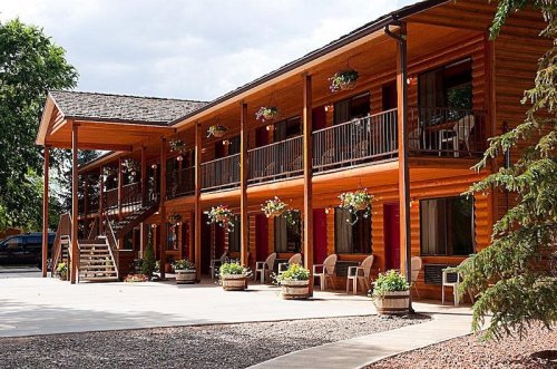 A wooden lodge with two stories, featuring balconies, flower pots, and a welcoming entrance.