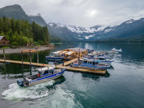 A scenic dock with several boats in a tranquil bay, surrounded by lush mountains and misty skies.