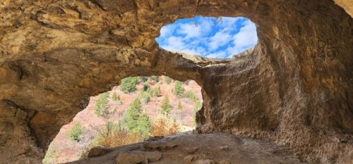 A rocky cave with two openings, revealing a blue sky and colorful trees in the background.
