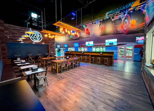Interior of a modern restaurant with wooden tables, a bar, and colorful lighting, featuring racing-themed decor.