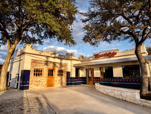 Exterior of Mama's Cafe, featuring a brick facade, large windows, and trees, under a partly cloudy sky.