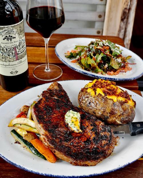 A grilled steak with butter, baked potato topped with cheese, and a fresh salad, accompanied by a glass of red wine.