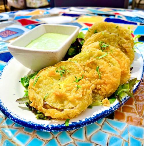 A plate of golden fried green tomatoes served with a creamy dipping sauce and garnished with herbs.