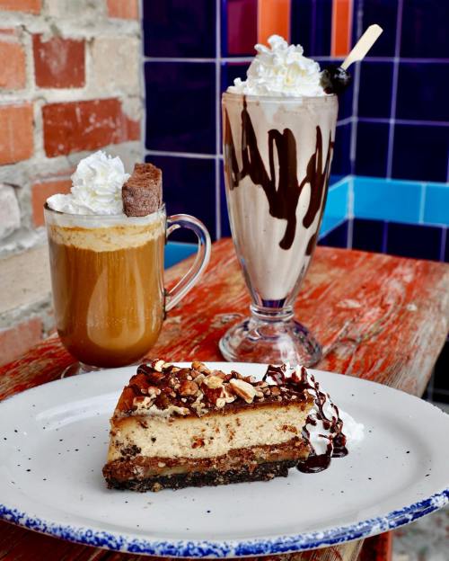 A slice of cheesecake topped with chocolate and nuts, alongside a coffee and a chocolate milkshake with whipped cream.