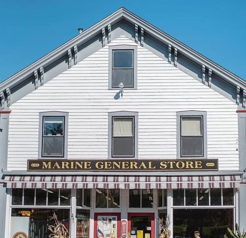 A charming white building with a sign reading "Marine General Store," featuring large windows and a striped awning.