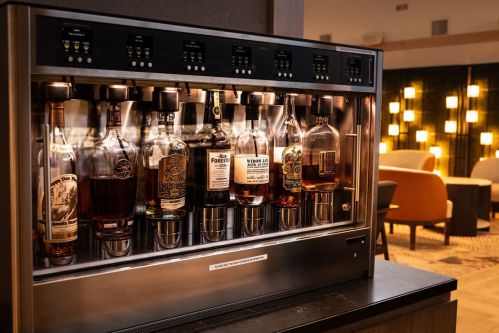 A sleek liquor dispenser with various whiskey bottles, set in a stylish lounge with soft lighting.