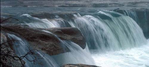 A serene waterfall cascading over rocky ledges, surrounded by mist and gentle waves.