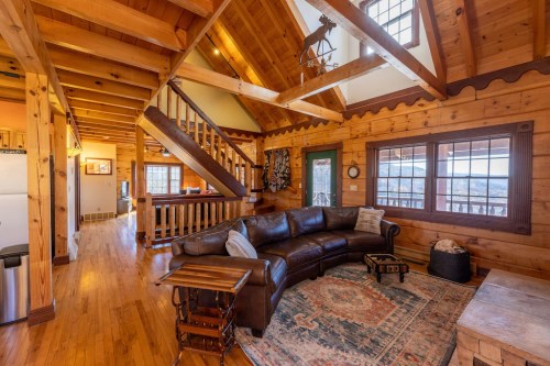 Cozy wooden cabin interior featuring a leather sofa, rustic decor, and a staircase leading to an upper level.