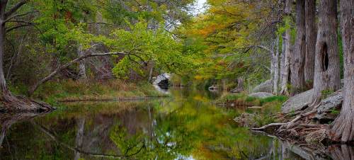 A serene river scene with trees reflecting in the water, showcasing vibrant autumn colors and a peaceful natural setting.