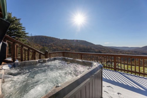 A hot tub on a deck with a scenic mountain view and bright sun in a clear blue sky. Snow covers the ground.