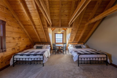 Cozy attic bedroom with two beds, wooden beams, and a small dining table by a window.