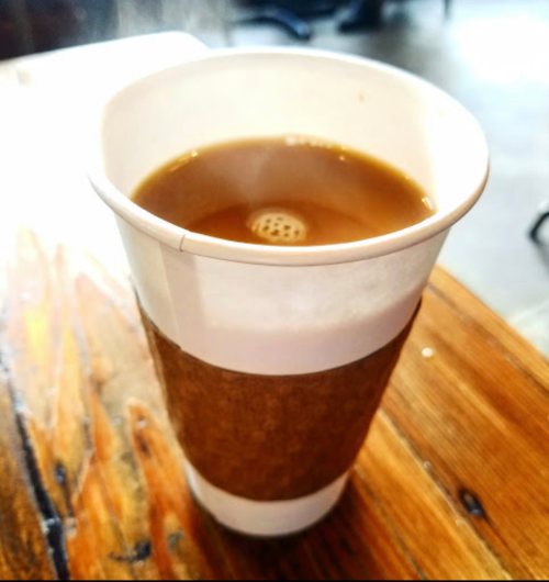 A close-up of a coffee cup with a cardboard sleeve, resting on a wooden table.