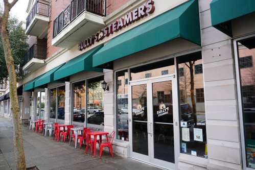 Exterior of Sully's & Steamers restaurant, featuring red chairs and green awnings on a city street.
