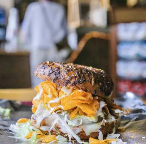 A close-up of a sandwich with a toasted bagel, filled with lettuce, cheese, and crunchy chips, on a foil surface.
