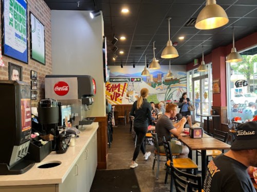 A casual restaurant interior with a soda fountain, patrons dining, and colorful murals on the walls.