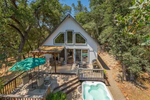 A cozy cabin with a deck, hot tub, and outdoor seating, surrounded by trees and nature.