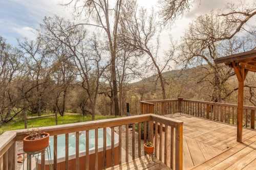 A wooden deck with potted plants overlooks a hot tub and a scenic landscape of trees and hills under a cloudy sky.