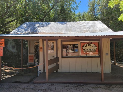 A wooden building with a corrugated metal roof, featuring a sign for Mercer Caverns and large windows.