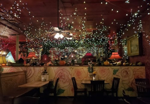 Cozy restaurant interior adorned with colorful fairy lights, floral wallpaper, and warm lamps, creating a festive atmosphere.