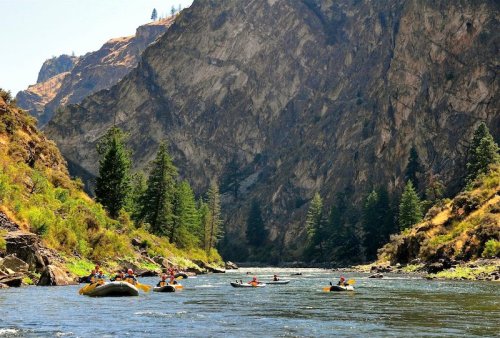 A group of people rafting on a river surrounded by steep, rocky cliffs and lush green trees.