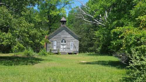 An old, weathered church surrounded by lush greenery and trees under a clear blue sky.