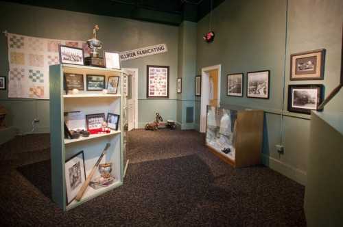 A museum display featuring a trophy, photographs, and artifacts in a green-walled room with a patterned carpet.