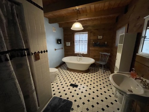 Cozy bathroom with a freestanding tub, wooden accents, black and white tiled floor, and natural light.