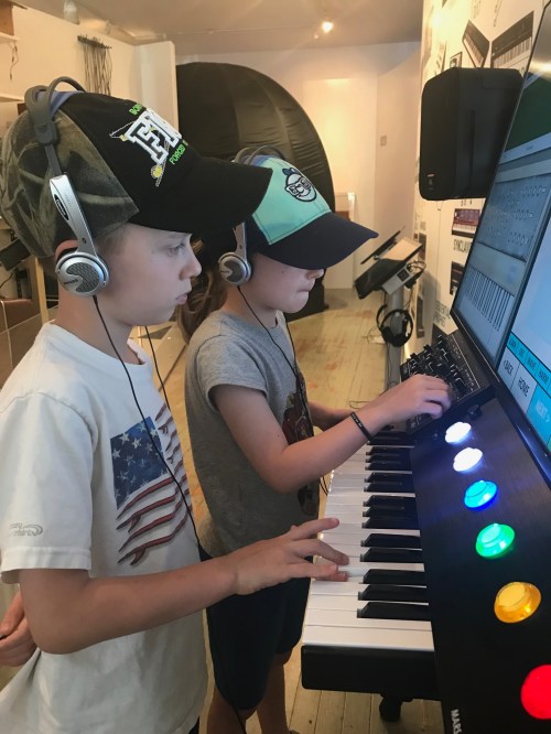 Two children wearing headphones play a digital keyboard, focused on the screen in front of them.