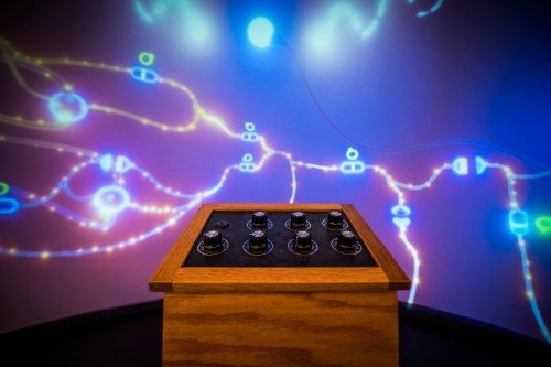 A wooden box with knobs sits in front of a colorful, illuminated wall displaying abstract light patterns.