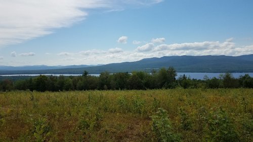 A scenic view of a lake surrounded by mountains and lush greenery under a partly cloudy sky.
