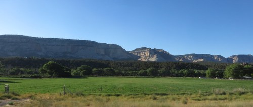 A scenic landscape featuring green fields in the foreground and rugged mountains under a clear blue sky.