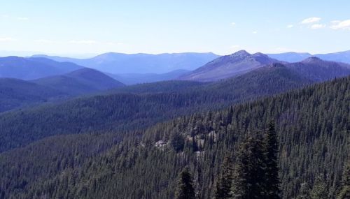 A panoramic view of lush green mountains under a clear blue sky, with distant peaks visible on the horizon.