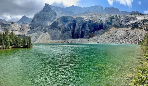 A serene lake surrounded by mountains, with clear green water reflecting the sky and rocky terrain.