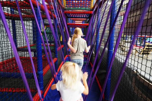 Two children navigate a colorful indoor play structure with nets and climbing areas.
