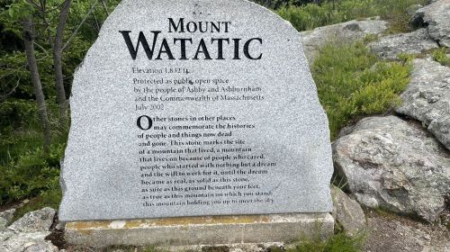 A stone monument for Mount Watatic, detailing its elevation and historical significance, surrounded by greenery.
