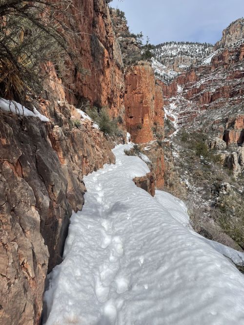 A snowy trail winds through rocky terrain, surrounded by red cliffs and a winter landscape.