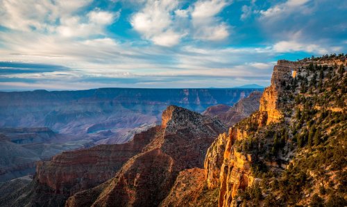 A stunning view of the Grand Canyon, showcasing layered rock formations and a vibrant sky with scattered clouds.