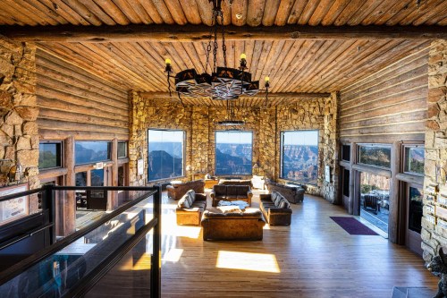 Spacious rustic living room with wooden beams, stone walls, and large windows showcasing a scenic view.
