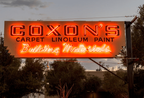 Neon sign for Coxon's Carpet, Linoleum, and Paint, advertising building materials against a twilight sky.