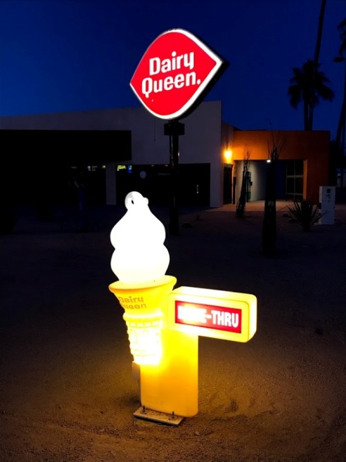 Dairy Queen sign at night featuring an illuminated ice cream cone and a "Drive-Thru" indicator.