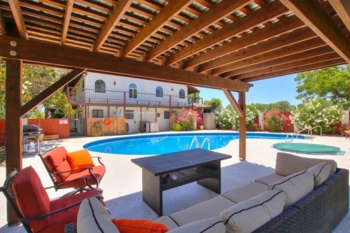 A cozy outdoor seating area with a table, overlooking a pool surrounded by greenery and a building in the background.