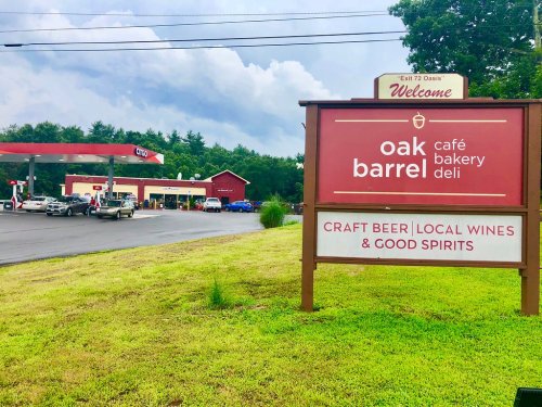 Sign for Oak Barrel Café, Bakery, and Deli, featuring craft beer, local wines, and good spirits, with a gas station nearby.