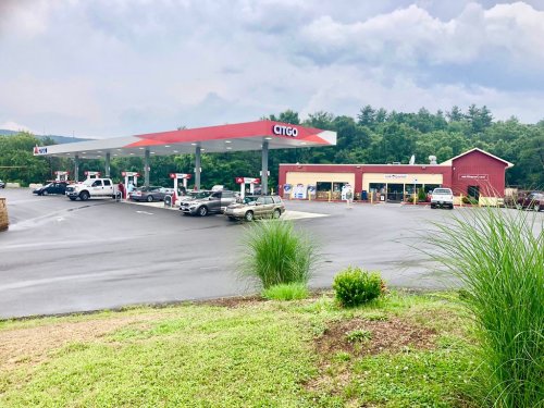 A CITGO gas station with several vehicles parked, surrounded by trees and a cloudy sky.
