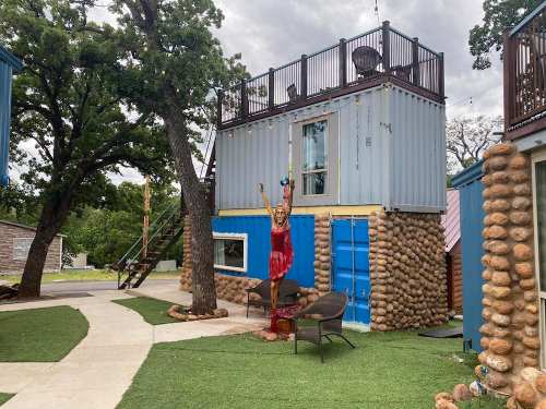 A colorful building made from shipping containers, featuring a statue of a woman in a red dress and a cozy outdoor seating area.